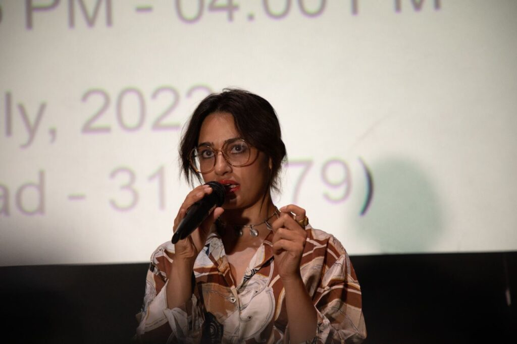 A person talking on microphone in front of theatre screen